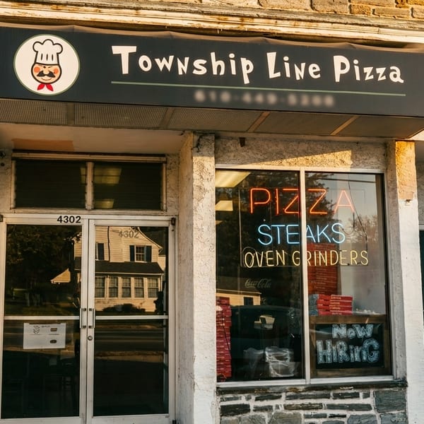 Exterior of Township Line Pizza, with a black awning and neon "PIZZA STEAKS" sign in the window.