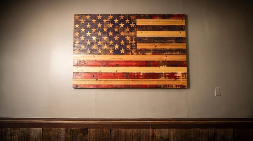 Rustic wooden American flag art hangs on a gray wall above dark wood paneling.