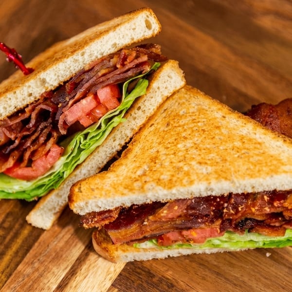Two halves of a toasted BLT sandwich with bacon, lettuce, and tomato on a wooden board.