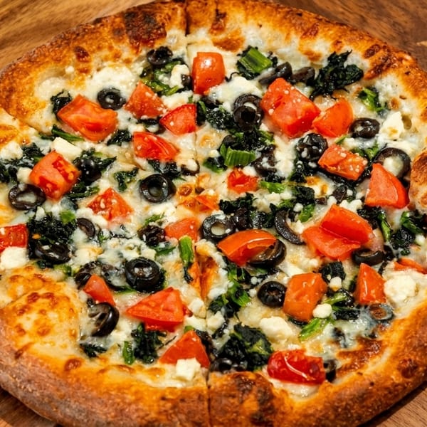 A whole pizza with spinach, black olives, diced tomatoes, and feta cheese on a wooden board.